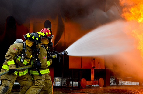 Two firefighters spraying a hose at a fire