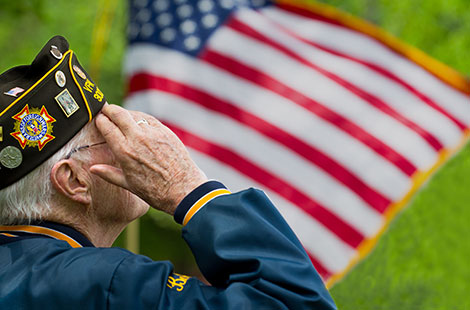 A veteran in uniform saluting with the American flag in the background