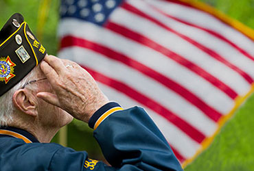 A veteran in uniform saluting with the American flag in the background